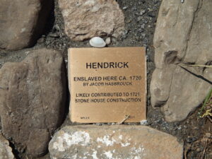Plaque honoring Hendrick's contribution to 1721 stone house construction, surrounded by rocks.