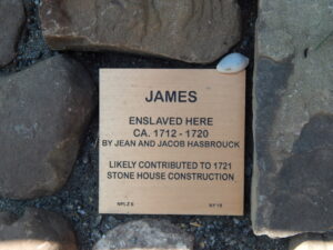 Plaque honoring James, enslaved ca. 1712-1720, contributor to 1721 stone house construction, surrounded by stones.